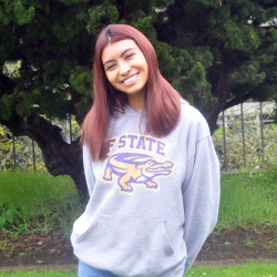 Sofia posing in front of tree wearing a light green SF State sweatshirt